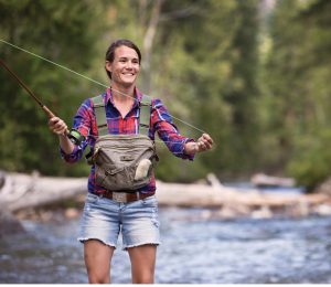 Woman smiling while fly fishing, standing in a river