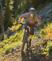 Man mountain biking in the forest on the uphill with gloves, backpack and sunglasses on