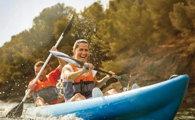 Two people in a kayak holding paddles laughing with trees in the background