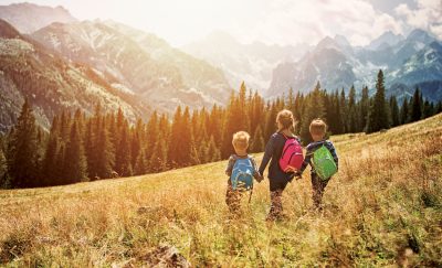 Three kids walking in a mountain prairie with backpacks